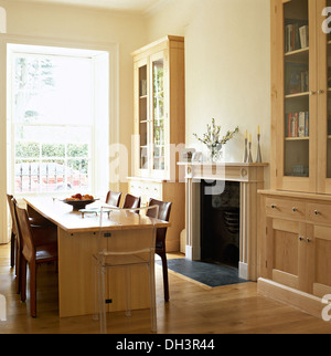 Blasse Holztisch und braunem Lederstühle im Speisesaal mit eingebauten Glas vorne Schränken auf beiden Seiten des Kamins Stockfoto