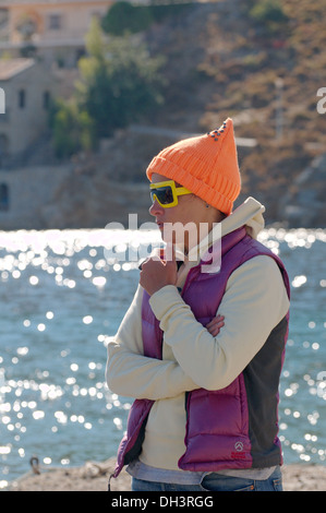 Frau in einem orangefarbenen Hut und gelbe Sonnenbrille steht an der Küste des Ägäischen Meeres. Griechenland, Insel Symi Stockfoto