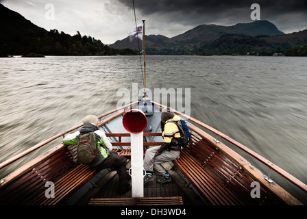 Der Bogen ein Ullswater Fähre mit zwei Wanderer saßen auf Bänken, wie es reist Ullswater Lake auf einem sehr bedeckt Spätsommer Tag. Stockfoto