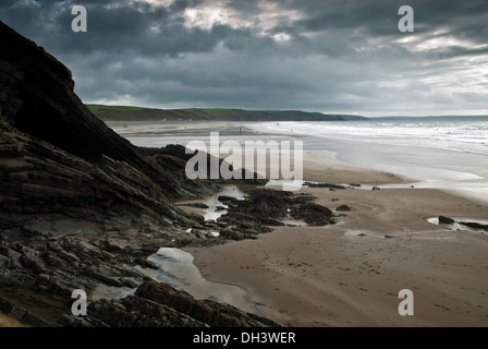 Newgale Sands in Pembrokeshire, Südwest-Wales umrahmt von einer felsigen Klippe und dramatischen Himmel bedeckt. Stockfoto