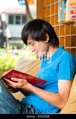 Asiatische Studentin - junger Mann sitzt auf dem Sofa lesen eine Buch oder Lehrbuch Lernen Stockfoto