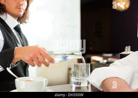 Coffeeshop - Barista Café mit einem Client, er trinkt Kaffee und die Kellner gießt Wasser in ein Glas Stockfoto