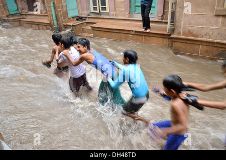 Jungs spielen in fließenden Monsun Regenwasser auf Straßen von Jodhpur Rajasthan Indien Stockfoto