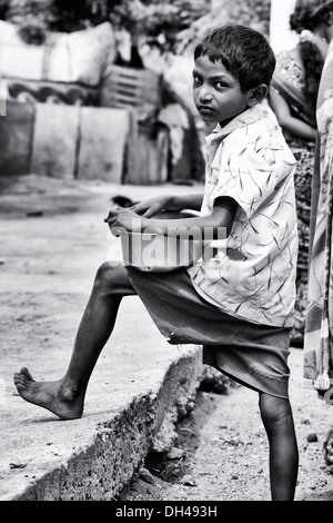 Niedrigere Kaste Indianerjunge mit einer Almosenschale draußen. Andhra Pradesh, Indien. Monochrom Stockfoto