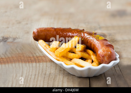 Beliebte deutsche Fastfood (Wurst mit Curry-Sauce) Currywurst und Pommes frites isoliert auf Holztisch Stockfoto