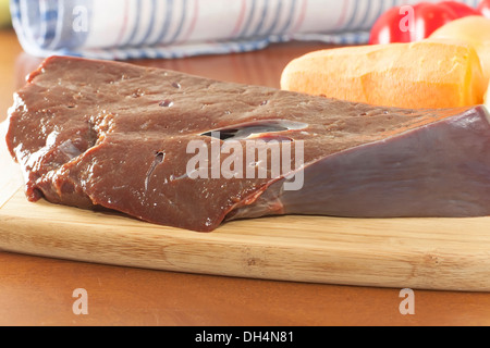 ein Stück rohe Rinderleber mit Gemüse auf dem Schneidebrett Stockfoto