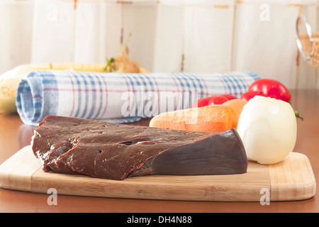 ein Stück rohe Rinderleber mit Gemüse auf dem Schneidebrett Stockfoto