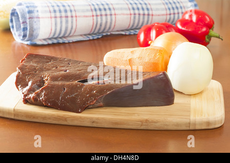 ein Stück rohe Rinderleber mit Gemüse auf dem Schneidebrett Stockfoto