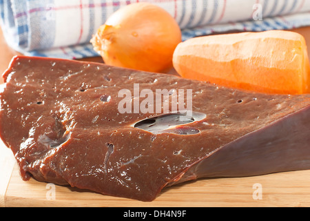 ein Stück rohe Rinderleber mit Gemüse auf dem Schneidebrett Stockfoto