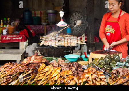 Horizontales Porträt einer Laodame in einem Restaurant am Straßenrand, das in Laos viel Fleisch vom Grill verkauft. Stockfoto