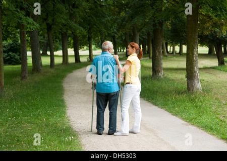 Frau und ein älterer Mann auf Krücken spazieren im park Stockfoto
