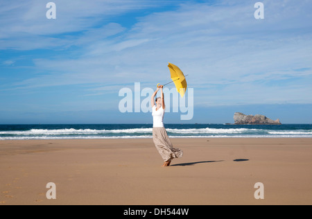 Frau zu Fuß mit einem Regenschirm auf einem windigen Strand Stockfoto