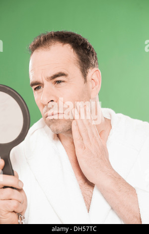 Mann trägt einen Bademantel beobachten sich selbst kritisch in einem Handspiegel, Mannheim, Baden-Württemberg, Deutschland Stockfoto
