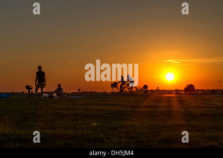 Paar beim Grillen am Flugplatz Tempelhof in der Abendsonne vor zwei vorbeifahrenden Radfahrer, Berlin-Tempelhof Stockfoto