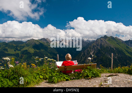 Frau sitzt auf einer Bank, Panoramablick, gesehen vom Walmendinger Horn Berg nach Osten, Allgäuer Alpen, Allgäu, Bayern Stockfoto