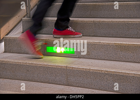 Person stürzte eine öffentliche Treppe mit einem grün beleuchteten Notausgangsschild, Deutschland Stockfoto