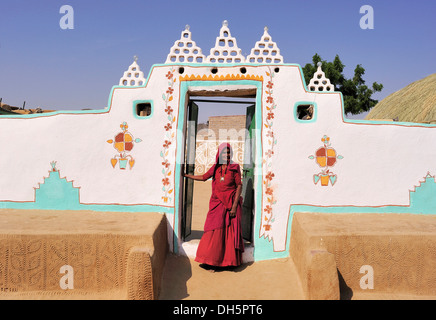 Traditionelle gemaltes Haus in der Thar-Wüste, eine indische Frau in einem roten Sari im Eingang, Thar-Wüste, Rajasthan, Indien, Asien Stockfoto