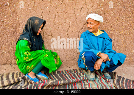 Älterer Mann und ein junges Mädchen, Berber Leute hocken auf einem Teppich oder Teppich vor einem Schlamm-Backstein-Haus reden Stockfoto