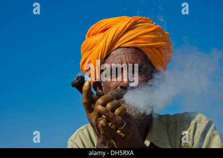 Rajasthani Senior mit einem orange Turban Rauchen eine Hash Pipe oder Hooka, Kamelmarkt,, Pushkar, Rajasthan, Indien Stockfoto