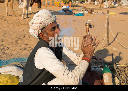 Indianer mit einem Turban sitzen auf dem Boden raucht eine Pfeife Hash, Pushkar Camel Fair, Pushkar, Rajasthan, Indien Stockfoto