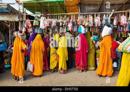 Indische Frauen in bunten Saris stehen vor einem Stall Verkauf von Spielzeug und Modeschmuck, Pushkar Camel Fair, Pushkar Stockfoto