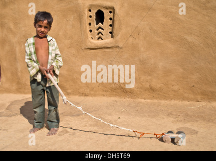 Junge spielt mit einem hausgemachten Spielzeugauto außerhalb ein Lehmhaus, Wüste Thar, Rajasthan, Indien Stockfoto