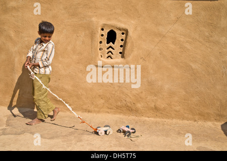 Junge spielt mit einem selbst gebastelten Spielzeugautos außerhalb ein Lehmhaus, Wüste Thar, Rajasthan, Indien Stockfoto