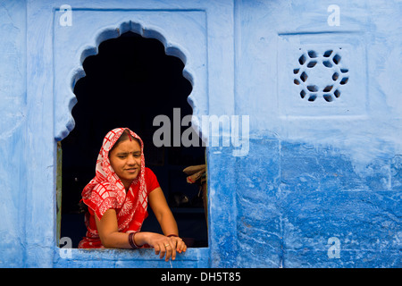 Junge indische Frau mit Kopftuch schaut aus dem Fenster eines blauen Wohnhauses, Jodhpur, Rajasthan, Indien Stockfoto