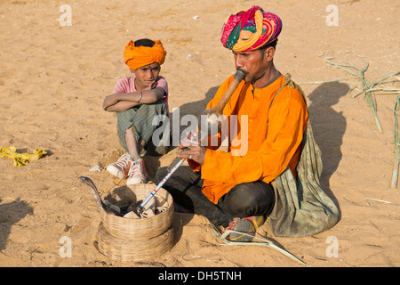 Rajasthani Schlangenbeschwörer mit einem Turban, eine Querflöte, eine Kobra oder Naja Wicklung aus einem Korb vor ihm zu spielen Stockfoto