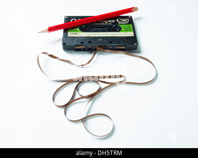 Super Dindy Audio-Kassette mit dem Klebeband, das auf einem weißen Tisch ausläuft und lockige, unordentliche Muster mit einem Bleistift bildet, um das Band aufzuwickeln Stockfoto