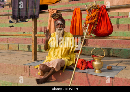 Ältere Sadhu, heiliger Mann oder Bummel durch asketische sitzt auf einer Decke auf den Stufen am Ufer des Flusses Ganges mit verschiedenen Stockfoto