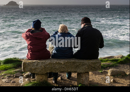 Drei ältere Menschen sitzen auf einer Granit-Bank mit Blick auf das Meer in Porth Nanven. Stockfoto