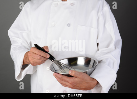 Nahaufnahme eines Kochs hält eine Edelstahl Schüssel und einen Schneebesen mischen. Querformat auf eine leichte bis dunkelgrauen Hintergrund. Stockfoto