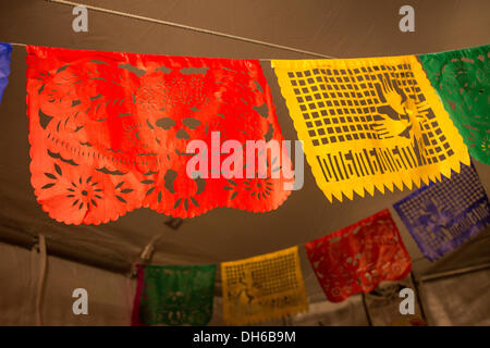 New York, NY, 31. Oktober 2013... Traditionelle Papier Ausschnitt Banner, genannt Papel Picado, hängen vom Zelt. Die rote Fahne zeigt einen Catrina, das Skelett Kopf einer Frau, die eine aufwendige europäisch anmutenden Hut. Bildnachweis: Ed Lefkowicz/Alamy Live-Nachrichten Stockfoto