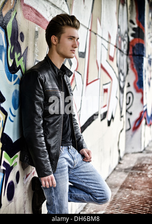 Attraktiven blonden Haaren junger Mann stehend gegen Graffitiwand Stockfoto