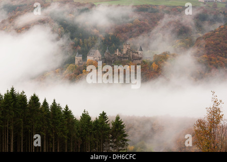 Mittelalterliche Burg von der anderen Seite des Tales aus gesehen, die von Nebel umhüllt ist. Schloss Bourscheid, Diekirch, Luxemburg. Stockfoto