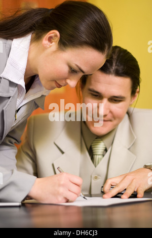 Frau unterzeichnet ein Dokument vor einem Mann Stockfoto