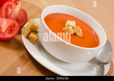 Tomatensuppe in Schüssel weiß & Platte auf Holztisch mit rohen Zutaten und croûtons Stockfoto