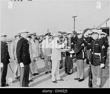 Präsident Harry S. Truman wird gesehen, wie er ein Gewehr an einen Marine zurückgibt, nachdem er es inspiziert hat, während andere Marines anwesend sind. Das Bild spiegelt die starke Führungsrolle von Truman bei militärischen Inspektionen nach dem Krieg wider. Stockfoto