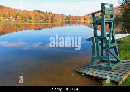 Ein Rettungsschwimmer Stuhl sitzt auf dem Rand der Barsch See in den Catskill Mountains mit einem reflektierten Himmel im Herbst in New York Stockfoto