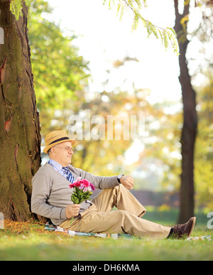 Ältere Gentleman mit Blumenstrauß sitzen auf einem grünen Rasen und überprüfen der Zeit, in einem park Stockfoto