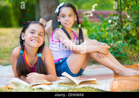 Zwei glückliche hispanische Schwestern lesen im park Stockfoto