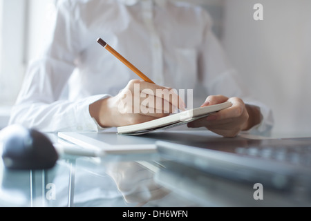 Zarte Frauenhand mit einem Bleistift in Anbetracht auf Merkzettel Stockfoto