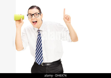Lächelnder Mann hören durch die Wand mit einer Tasse Stockfoto
