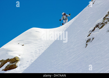 Skifahrer vor den steilen, schneebedeckten Hang gegen den klaren, blauen Himmel Stockfoto