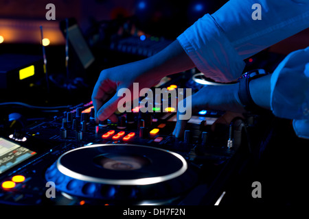 Nahaufnahme von den Händen der männlichen Discjockey Mischen von Musik auf seinem Deck mit seinen Händen balanciert über die Vinyl-Schallplatte auf die Drehscheibe und die Steuerschalter in der Nacht. Stockfoto