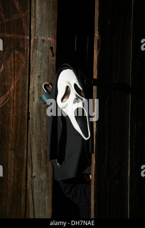 Mann in beängstigend "Schrei" Maske hält Axt. Maske der Sensenmann. Weißen Geistermaske Karneval und schwarze Kapuze. Scary Movie Film. Stockfoto