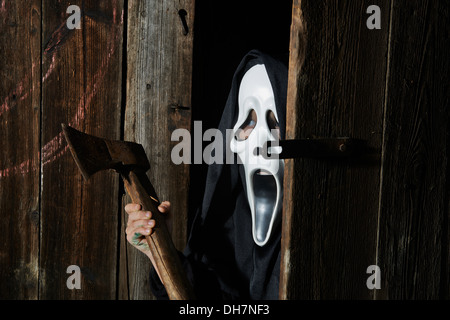 Mann in beängstigend "Schrei" Maske hält Axt. Maske der Sensenmann. Weißen Geistermaske Karneval und schwarze Kapuze. Scary Movie Film. Stockfoto