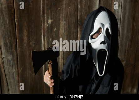 Mann in beängstigend "Schrei" Maske hält Axt. Maske der Sensenmann. Weißen Geistermaske Karneval und schwarze Kapuze. Scary Movie Film. Stockfoto