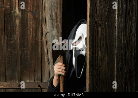 Mann in beängstigend "Schrei" Maske hält Axt. Maske der Sensenmann. Weißen Geistermaske Karneval und schwarze Kapuze. Scary Movie Film. Stockfoto